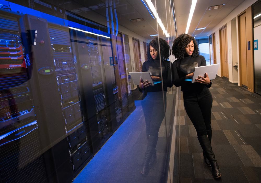 An engineer with a tablet walking beside racks of servers